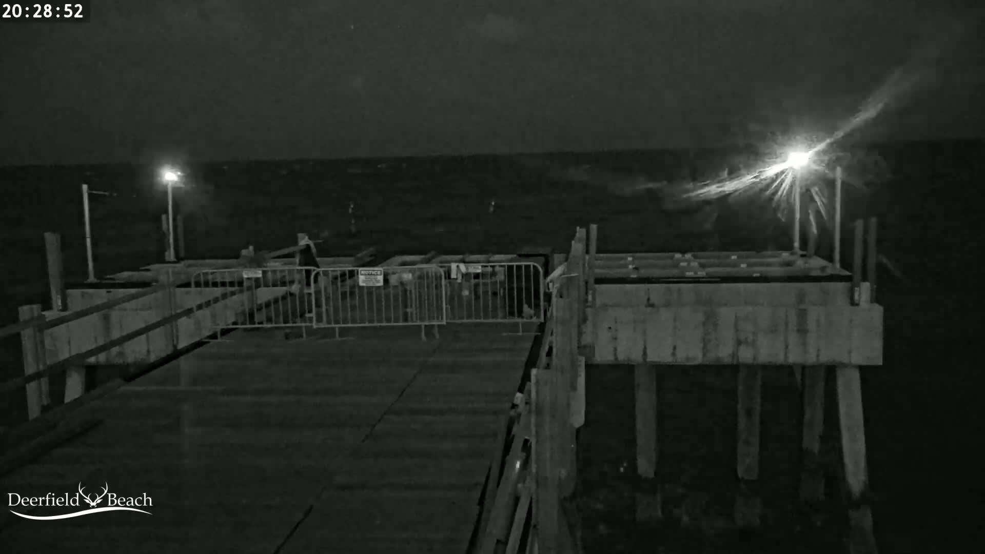 A nighttime, low-light image shows a pier extending over a choppy body of water under a dark sky.