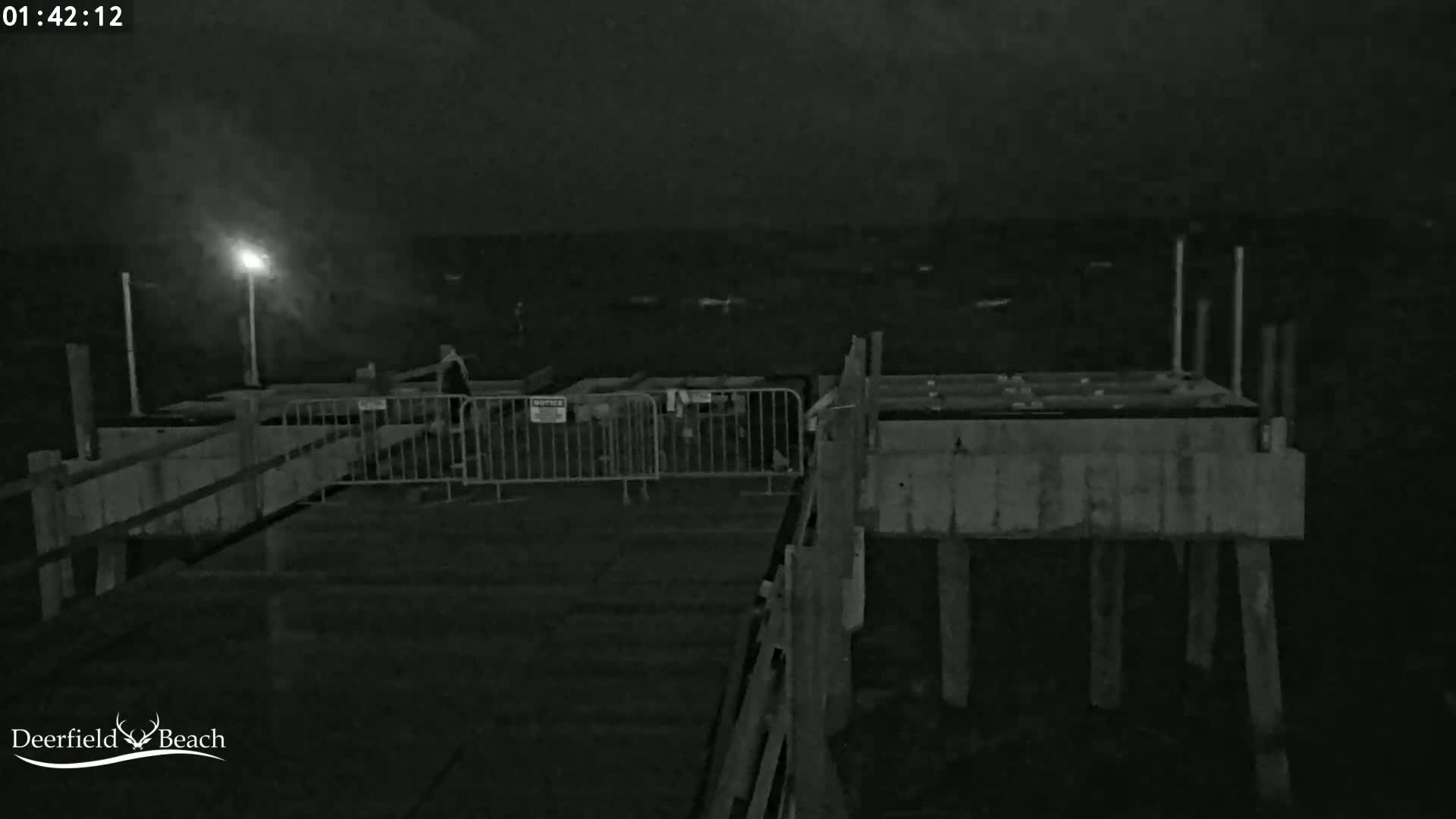 A nighttime, low-light image shows a section of a pier or boardwalk with metal barriers and some structures under construction.