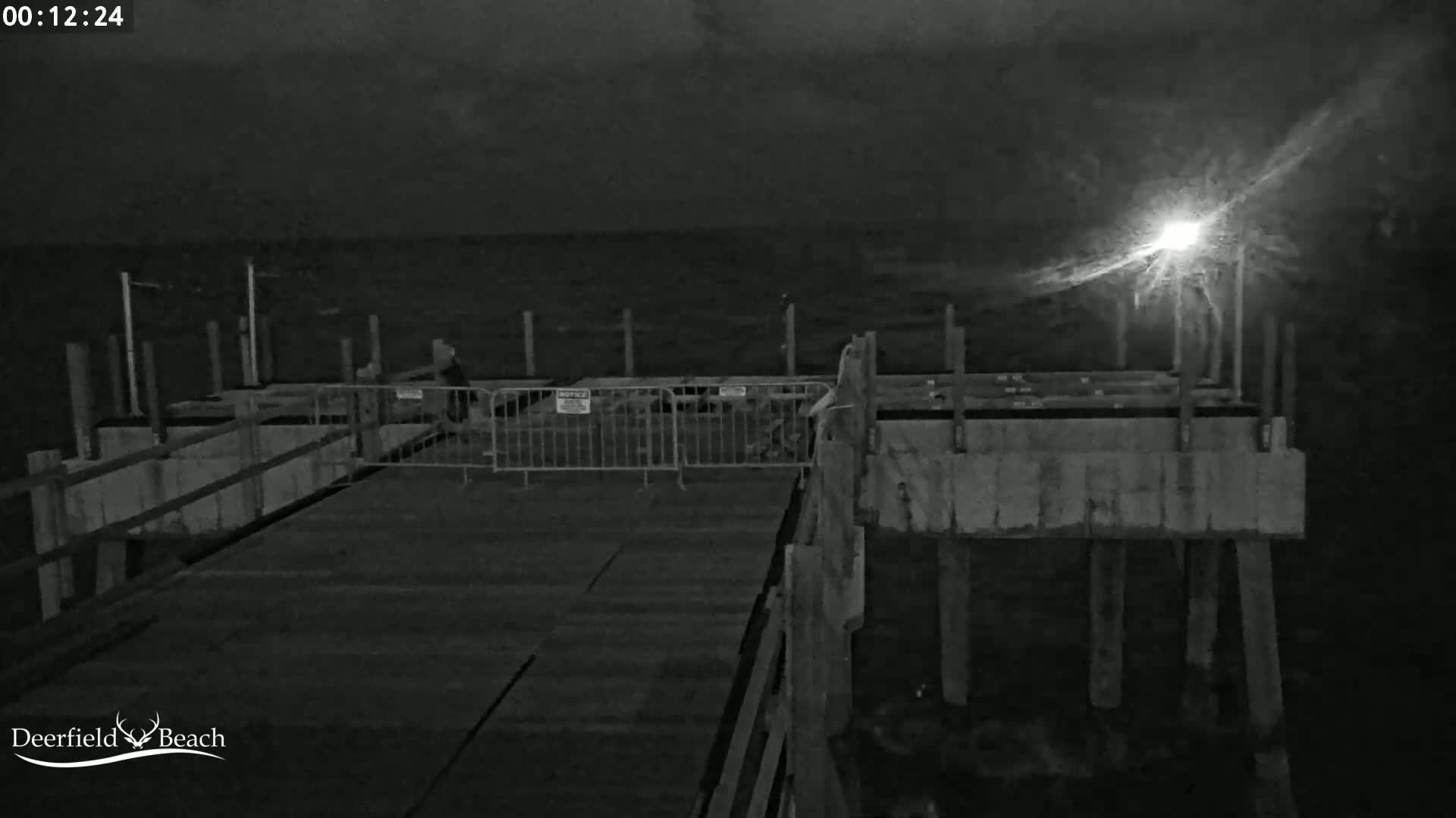 A nighttime, low-light view of a pier extending over dark water, partially blocked off by metal barriers.