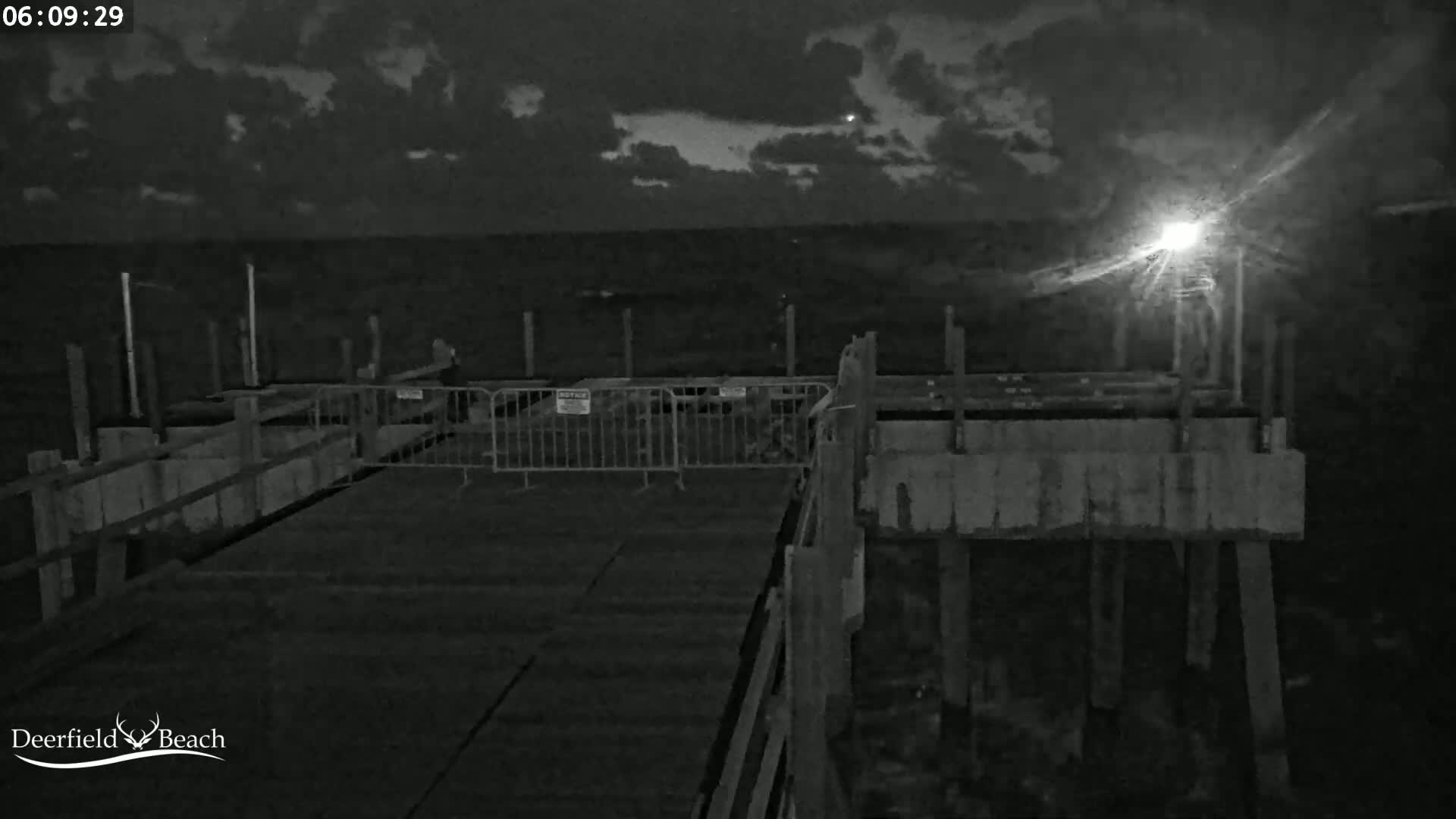 A nighttime view of a dark, partially constructed pier over dark water under a cloudy sky.