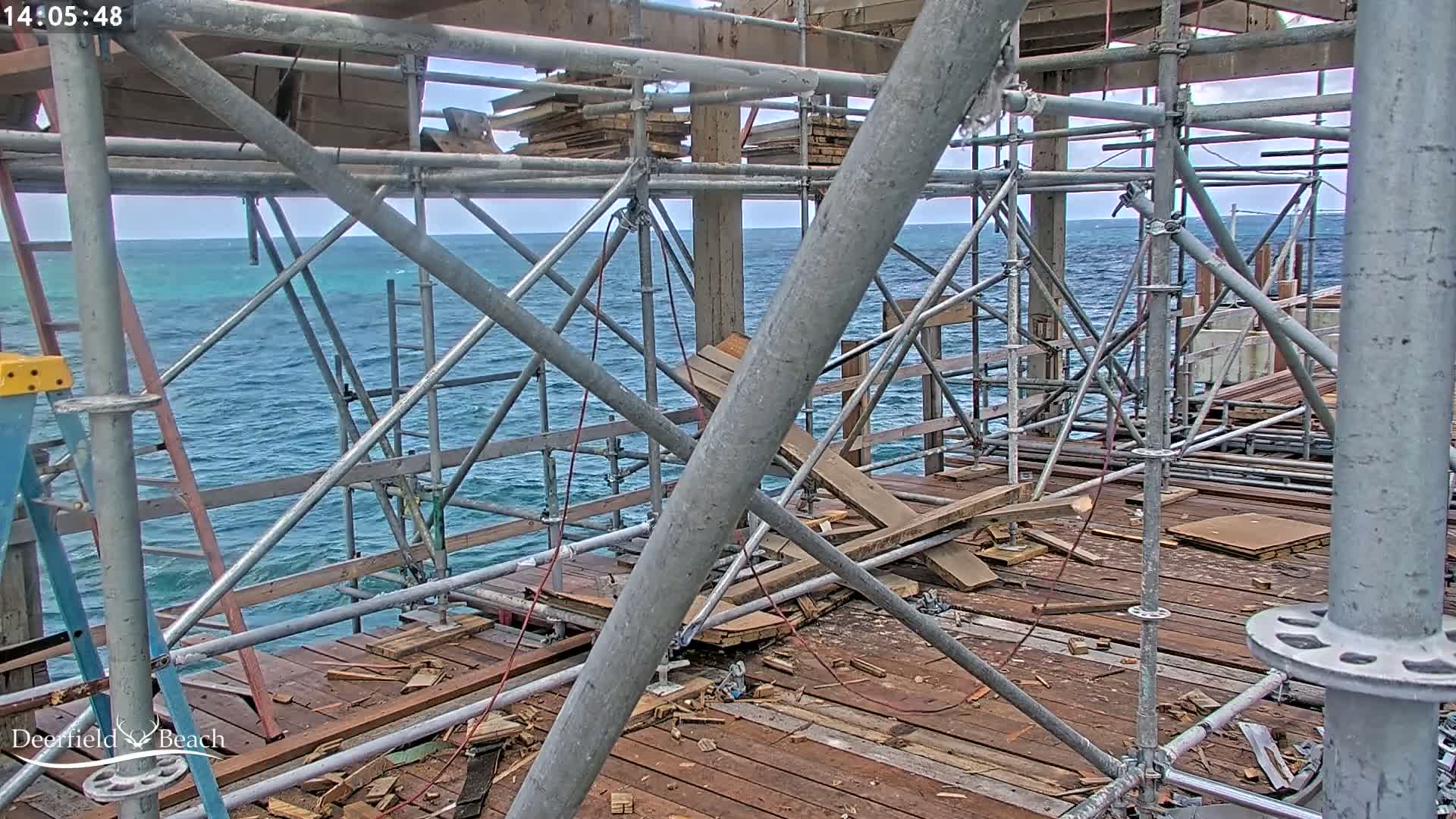 A partially constructed pier, under scaffolding, overlooks a choppy ocean under an overcast sky.