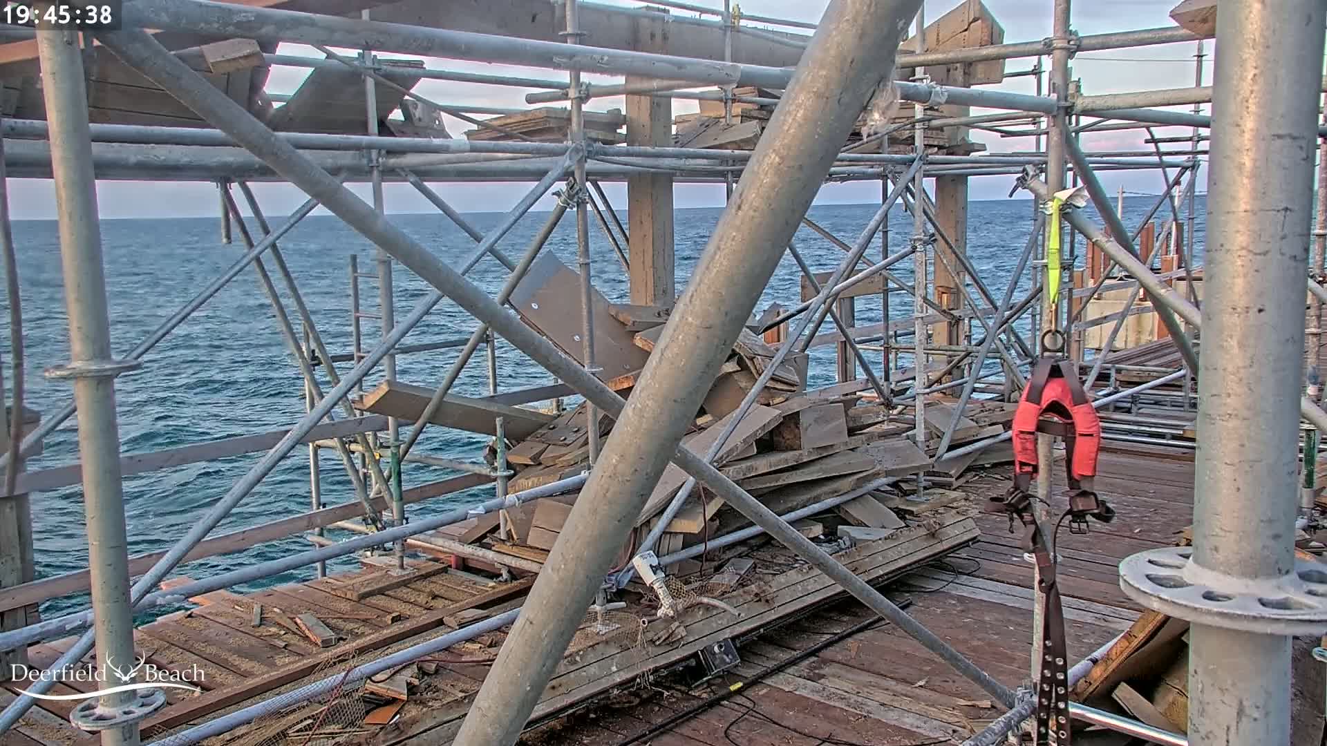 A partially constructed structure over a calm ocean is surrounded by scaffolding and debris.
