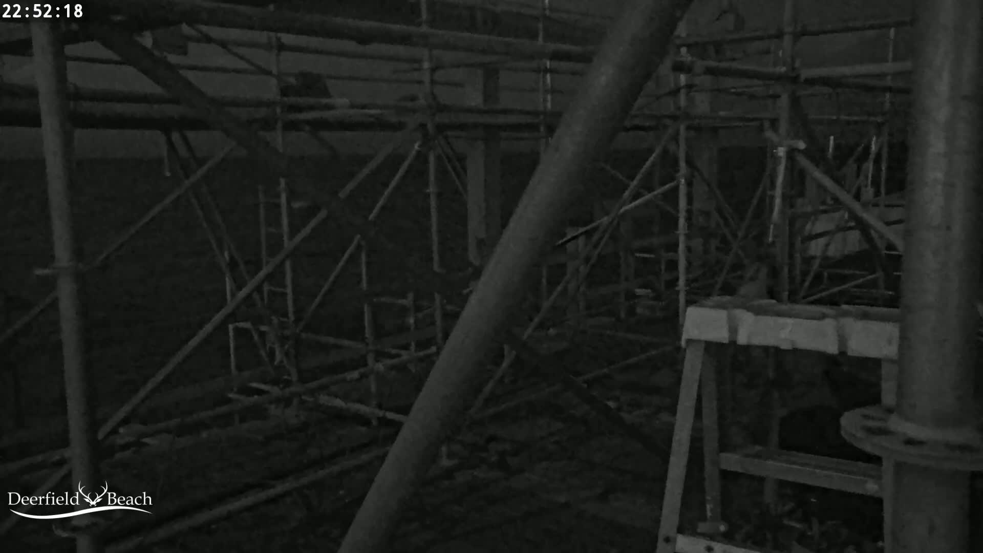 A nighttime, low-light image shows a complex network of scaffolding and metal structures.