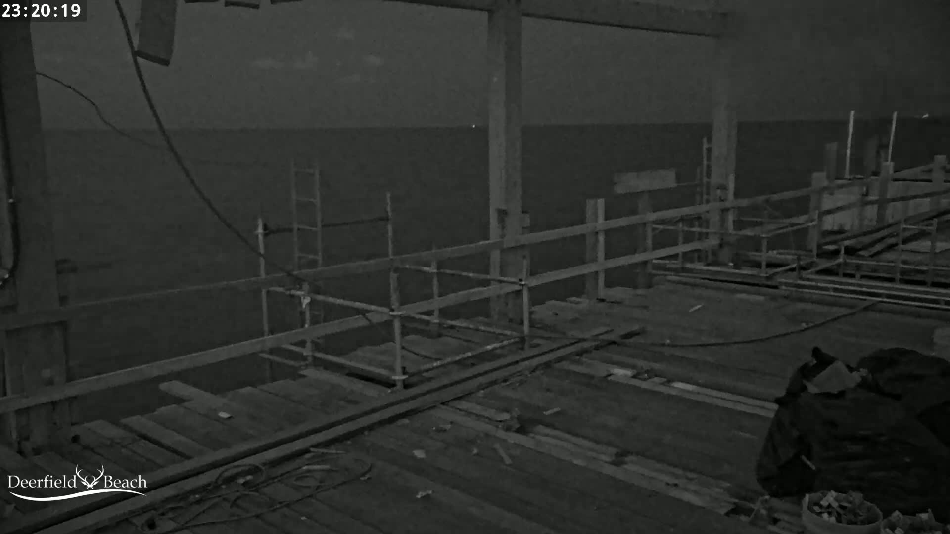 A nighttime, low-light image shows a partially constructed pier extending over a dark body of water under a mostly clear sky.