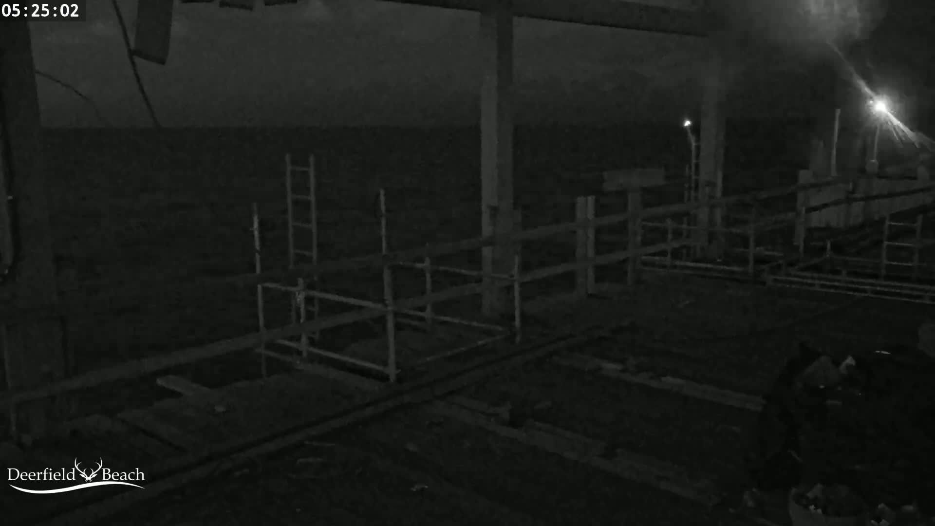 A dark, nighttime view of an outdoor structure with metal railings and scaffolding, overlooking a body of dark water.