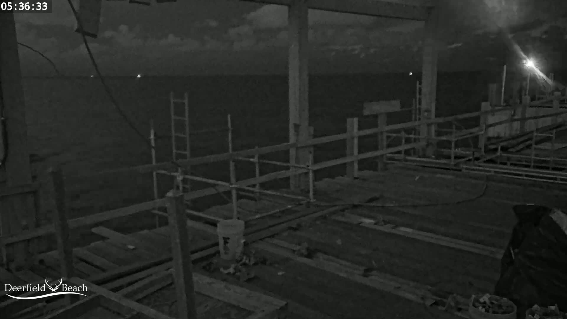 A nighttime view of a partially constructed pier extends over dark water under a cloudy sky.