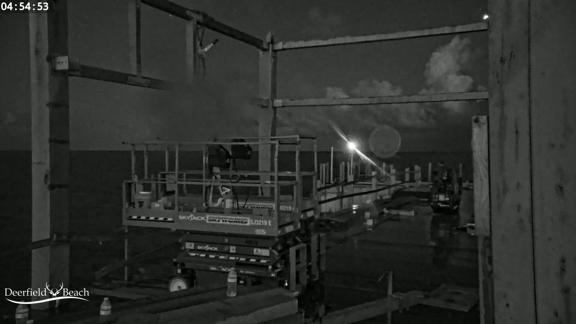 A nighttime, cloudy scene shows an elevated work platform near a body of water with a pier under construction.