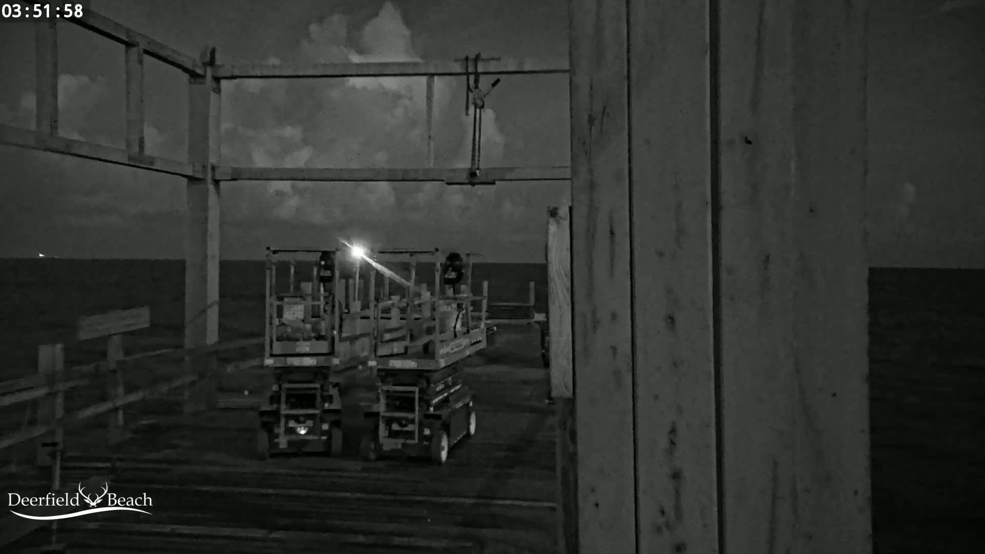 Two elevated work platforms are parked on a pier at night under a partly cloudy sky.