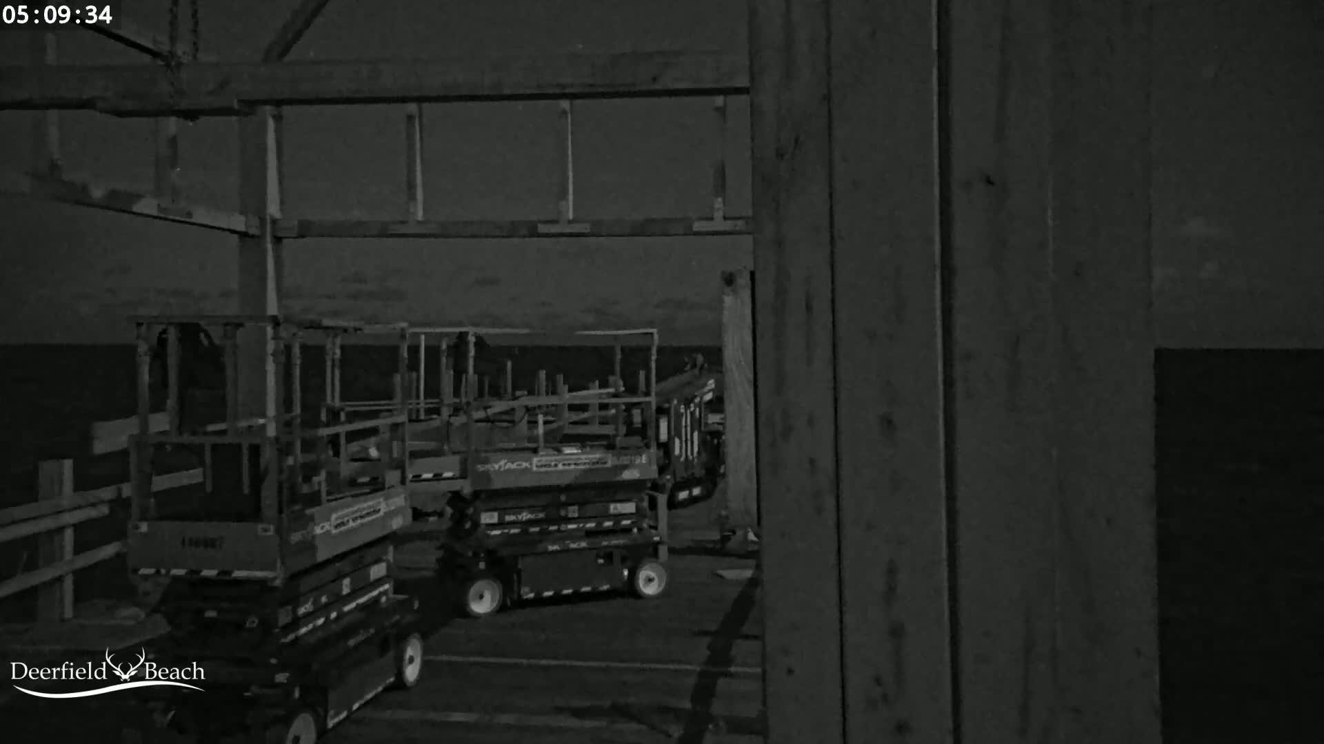 Under a dark night sky, several pieces of construction equipment are parked near a wooden structure.