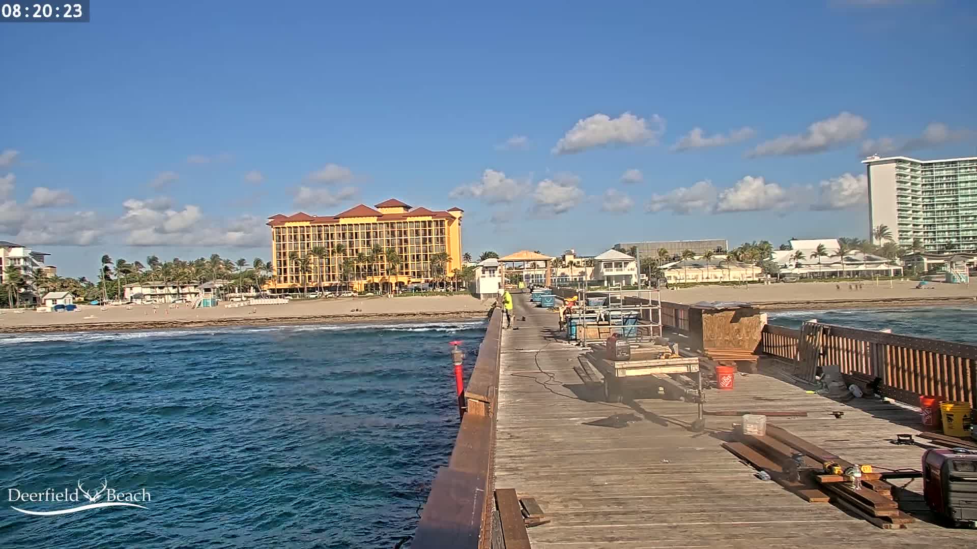 A partly cloudy day reveals a beach scene with a large hotel, several smaller buildings, and a pier under construction.