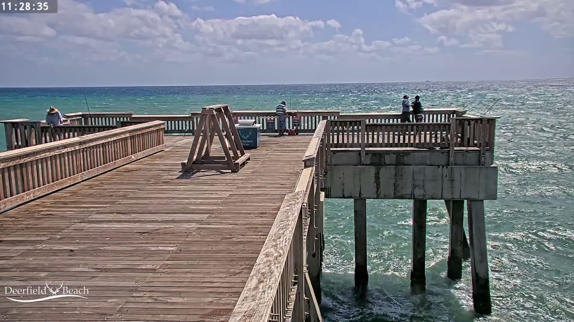 A brightly lit wooden pier, glistening from what appears to be recent rain, extends over dark water under a heavily overcast night sky.