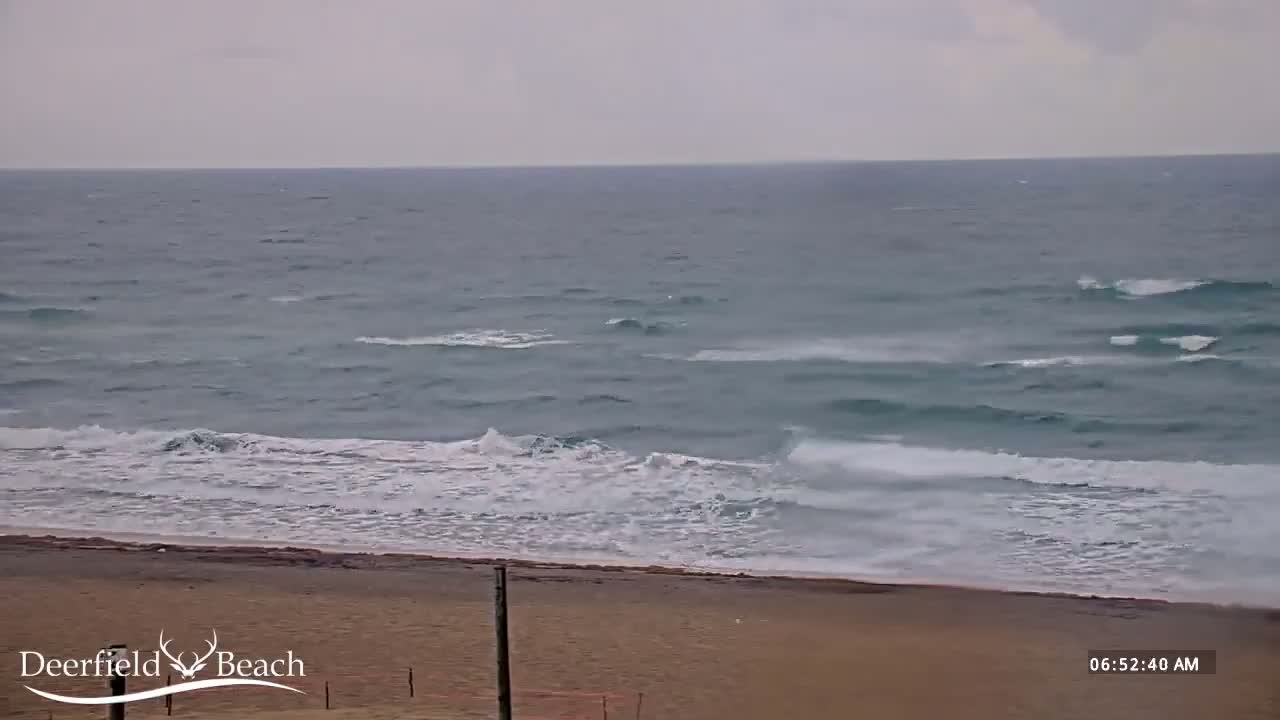 A sandy beach with moderate waves rolling onto the shore under an overcast sky.