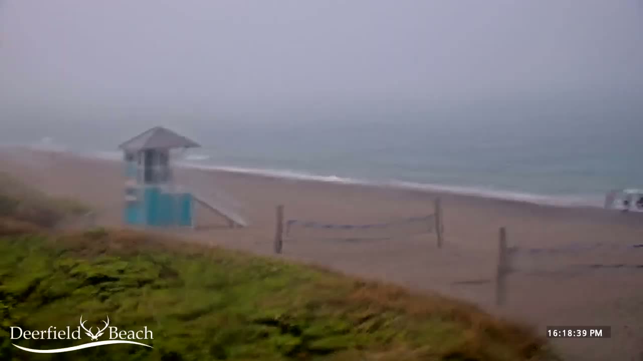 A lifeguard stand sits on a beach during a heavy rain and overcast day, with a volleyball net visible in the background.