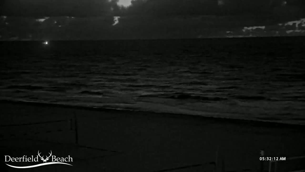 A dark, nighttime beach scene shows a gently rolling ocean under a cloudy sky.