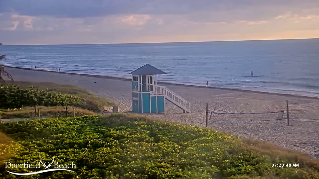 A teal and white lifeguard stand sits on a sandy beach overlooking a calm ocean under a partly cloudy sky.
