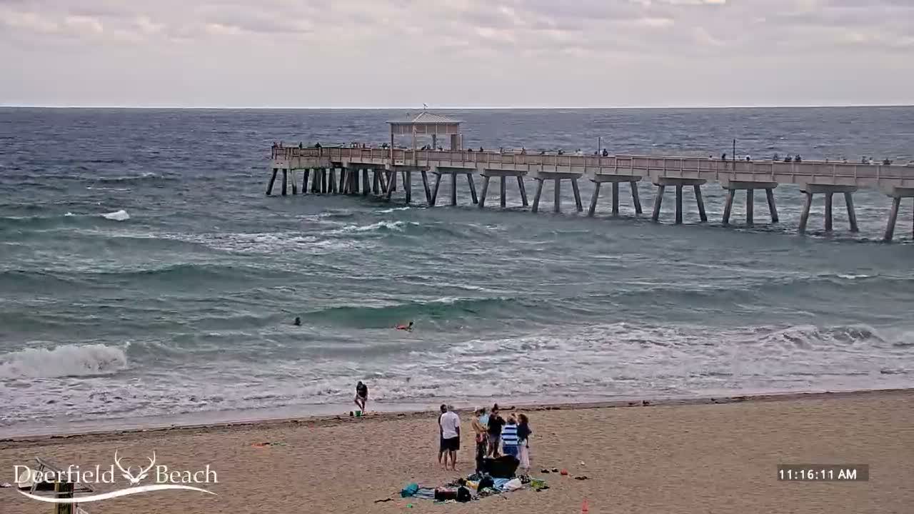 A small boat with a bright, star-like light shining from its top casts a shimmering reflection on calm water under a clear, dark night sky.