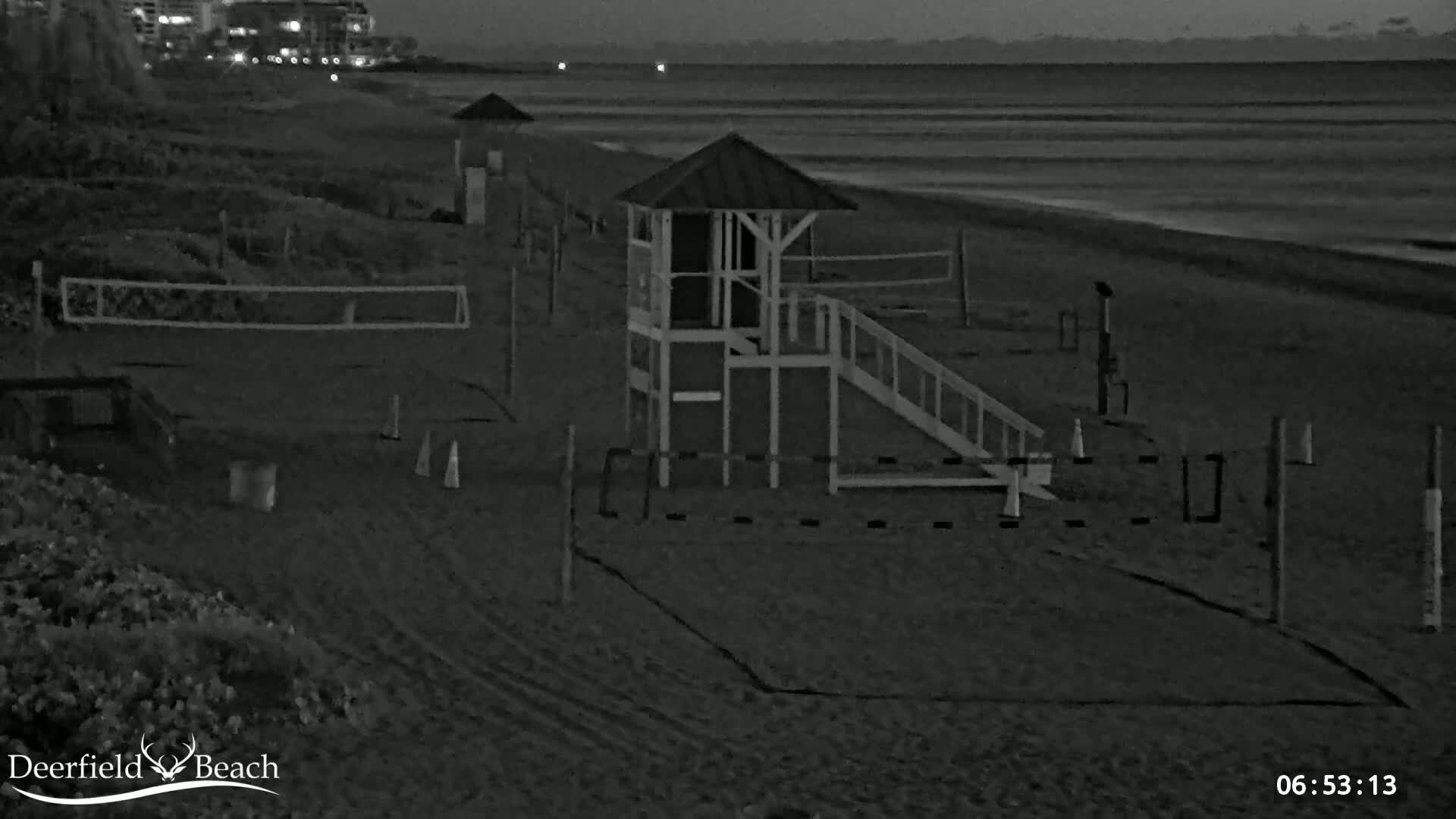 A dark beach at night shows a lifeguard stand, volleyball nets, and some cones near the water.