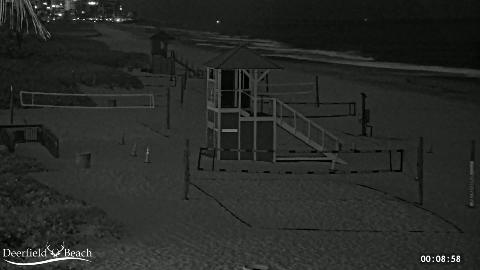 A nighttime beach scene shows several volleyball nets and a lifeguard stand on a sandy beach with calm ocean waves in the background.