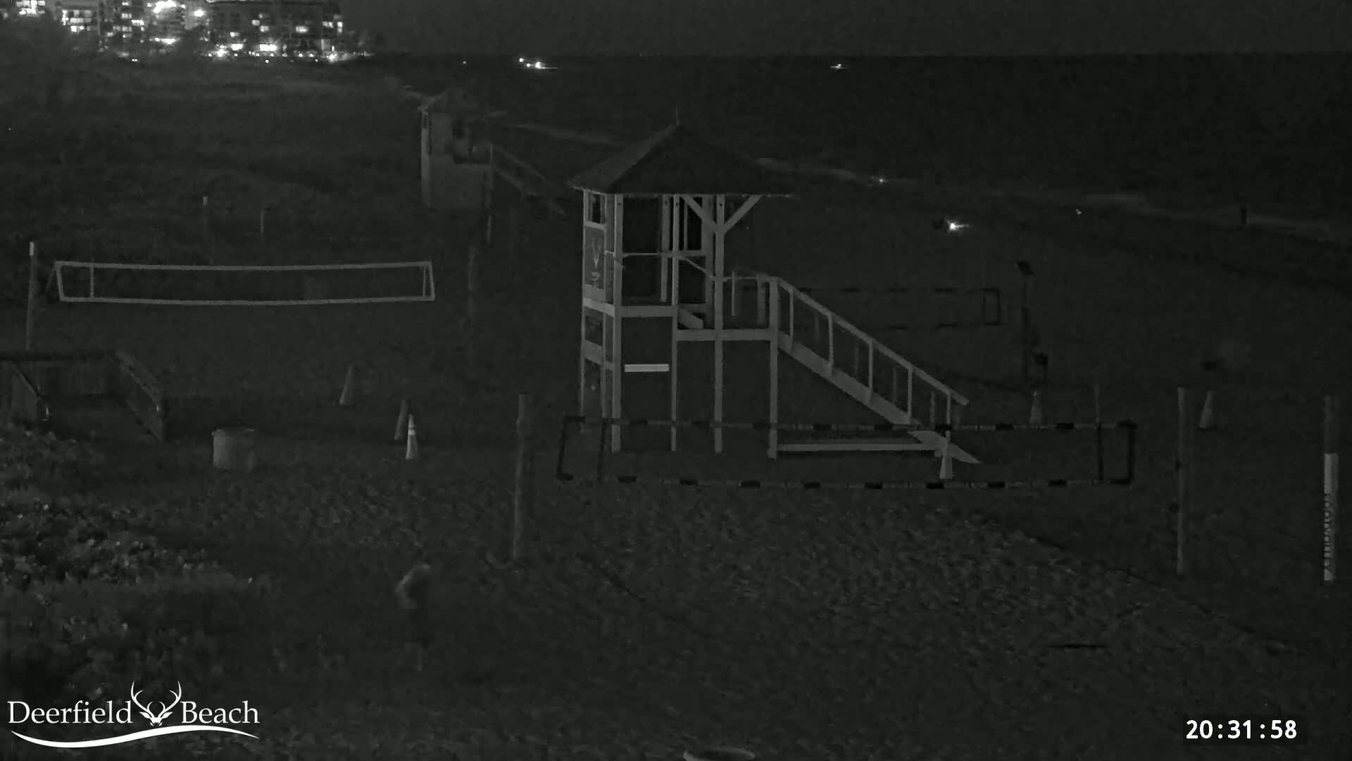 A nighttime beach scene shows a lifeguard stand, volleyball nets, and a dark ocean under a clear sky.