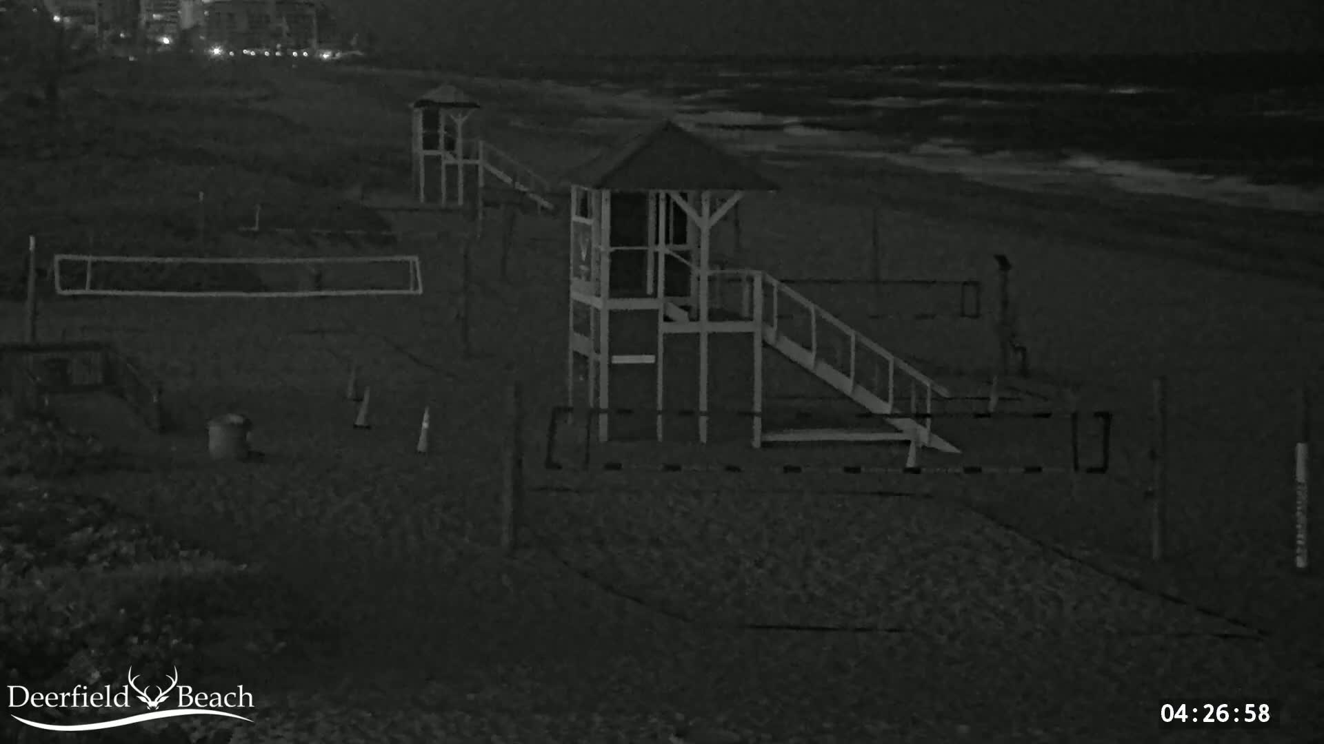A nighttime view of a beach with two lifeguard stands, a volleyball net, and gently rolling waves.