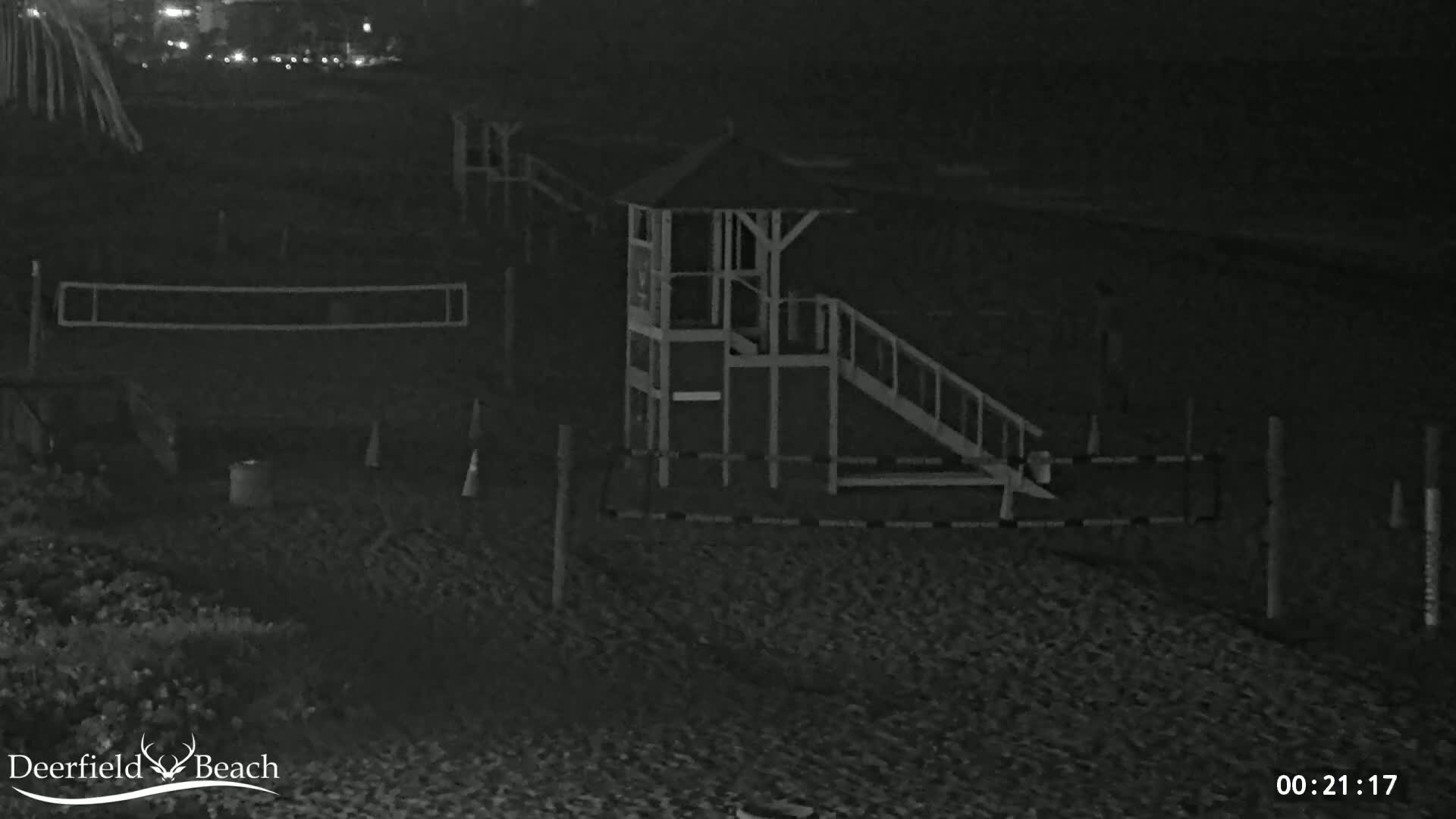 A nighttime, low-light image shows a lifeguard stand, volleyball net, and other beach equipment on a sandy beach.
