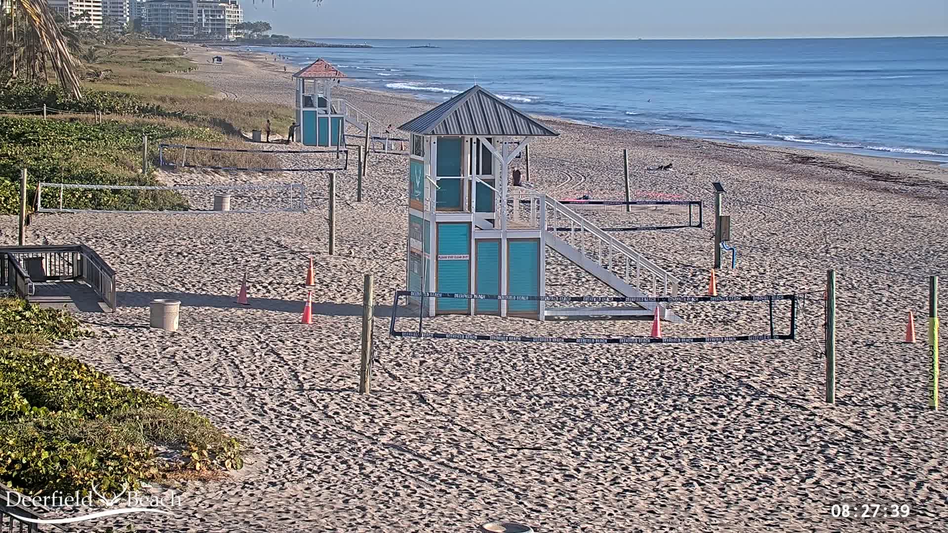 A sandy beach with lifeguard stands, volleyball nets, and calm ocean under a clear sky.