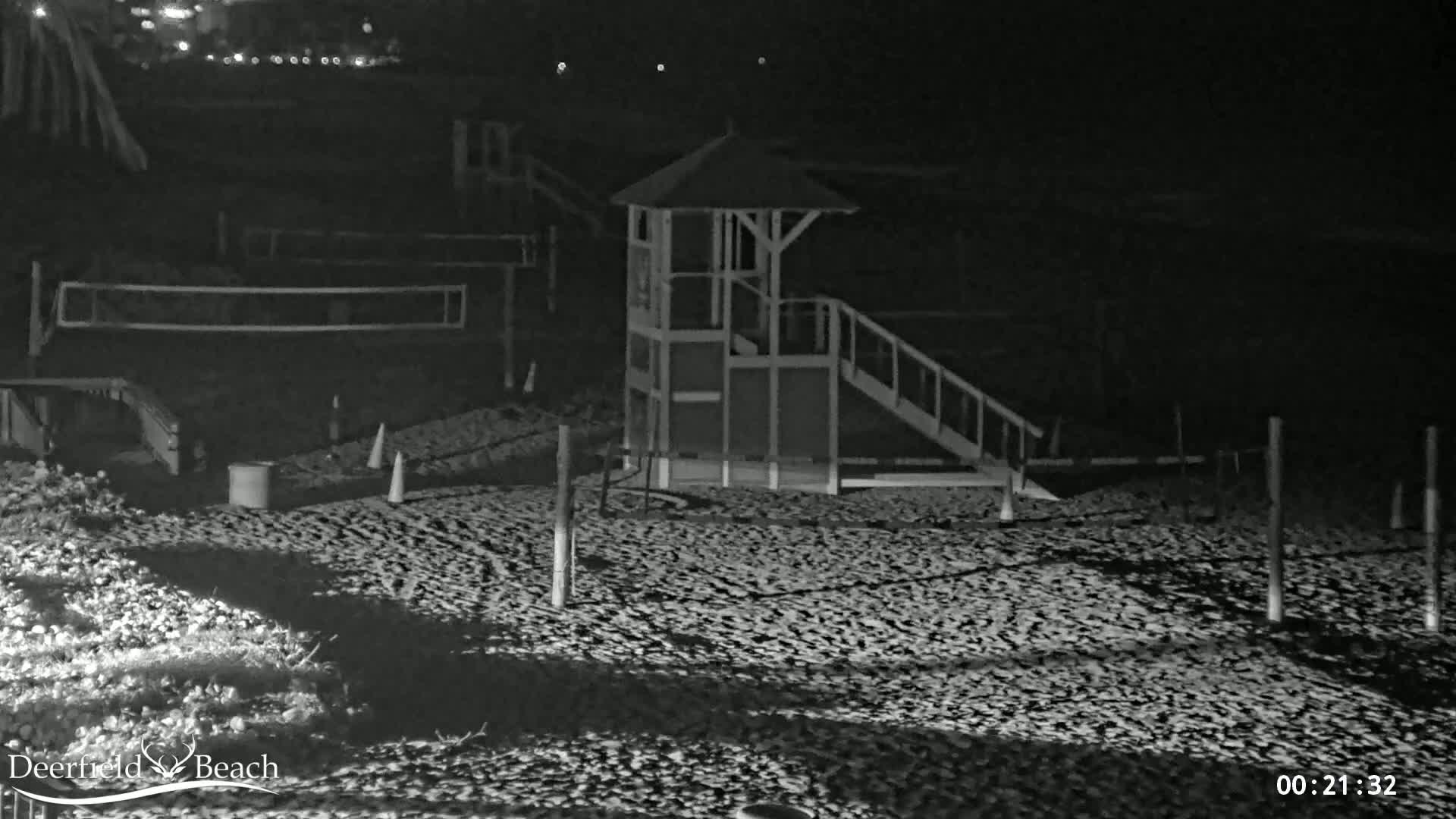 A lifeguard stand with a slide sits on a dark, sandy beach at night.