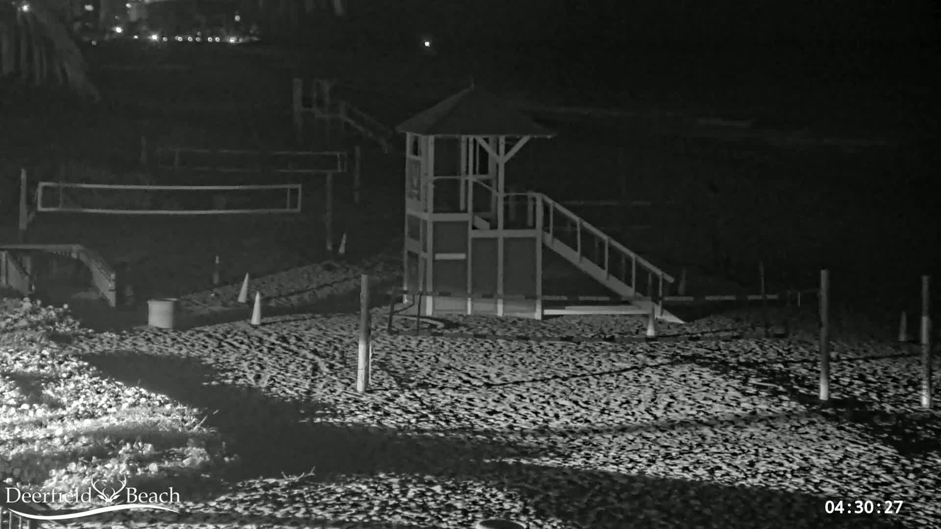 A nighttime beach scene shows a lifeguard stand with a ramp, volleyball nets, and some low lighting.