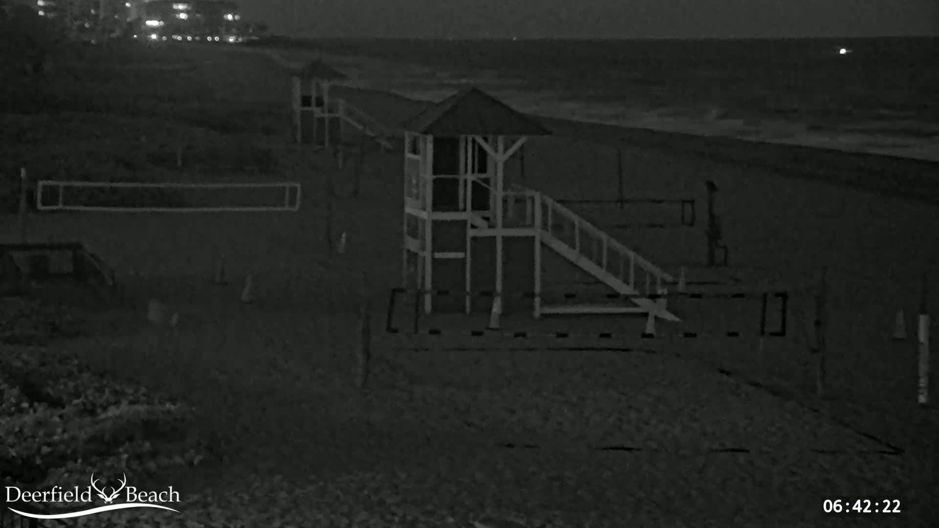 A lifeguard stand with a ramp sits on a dark, sandy beach at night, with a calm ocean in the background.