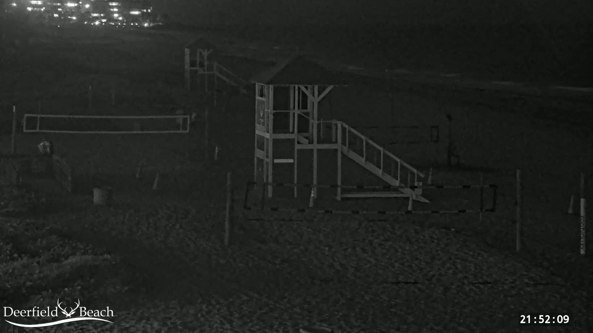 A nighttime, low-light image shows a lifeguard stand and volleyball net on a sandy beach.