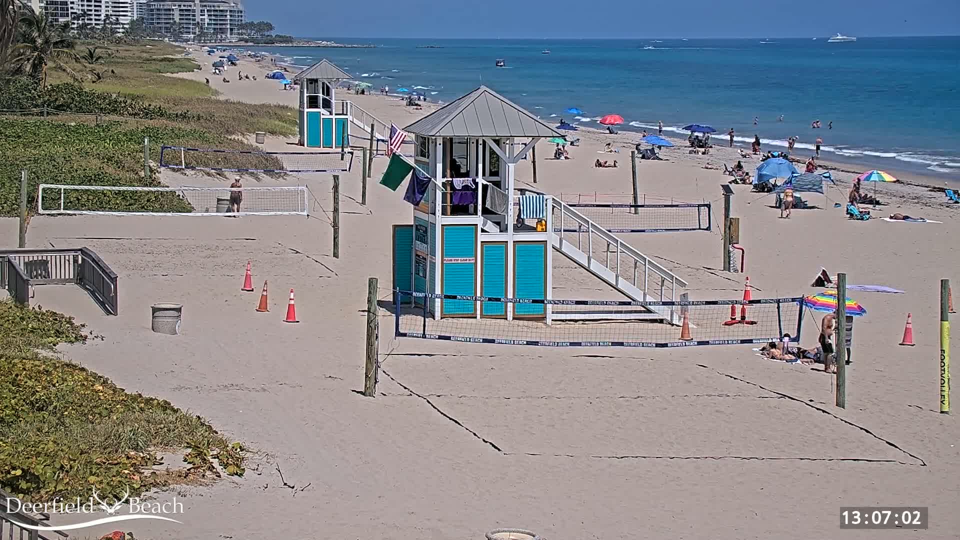 A sandy beach with volleyball courts, lifeguard stands, and people enjoying a sunny day on the ocean.