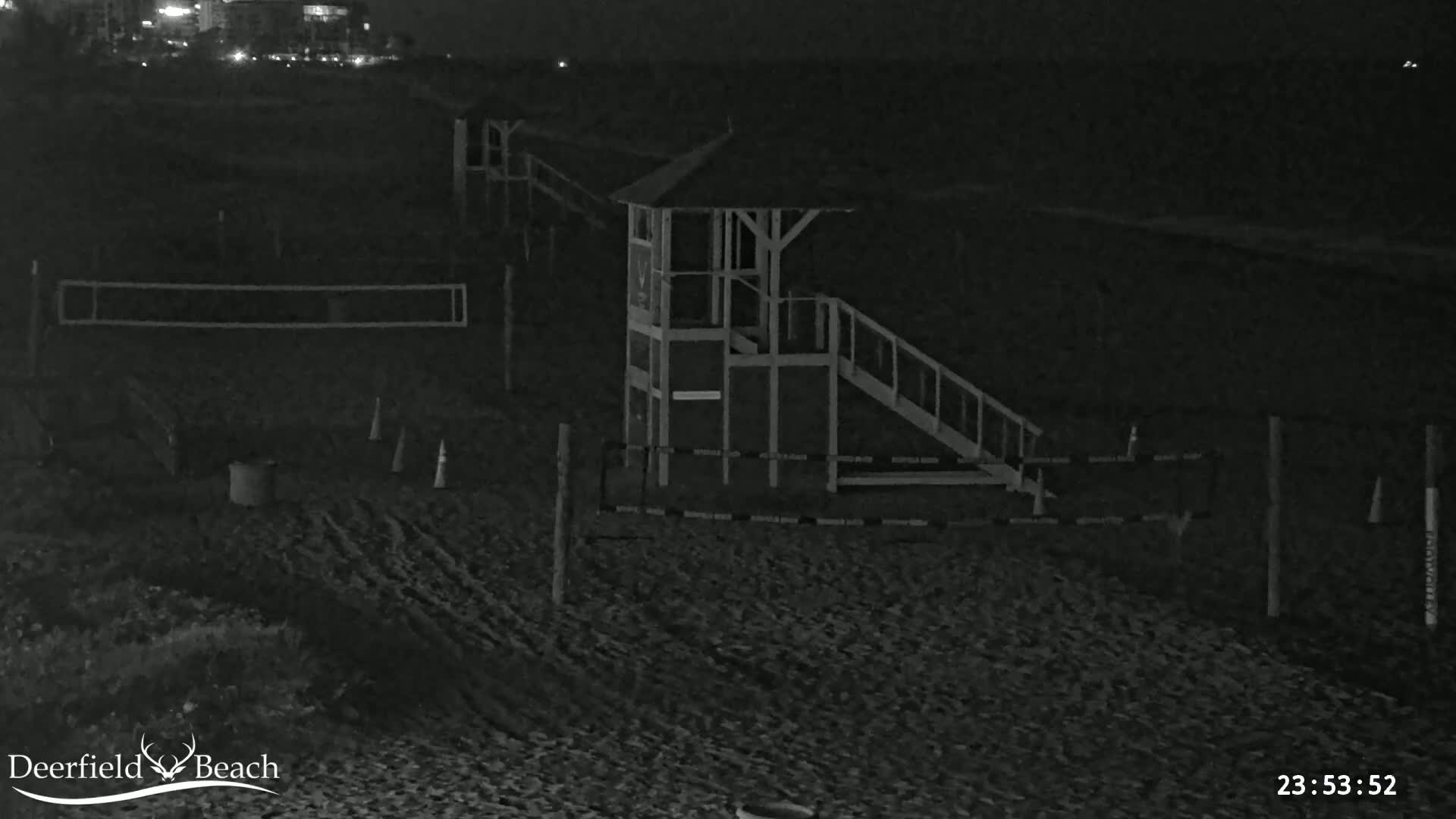 A nighttime, black and white view of a beach volleyball court and lifeguard stand on a dark sandy beach.