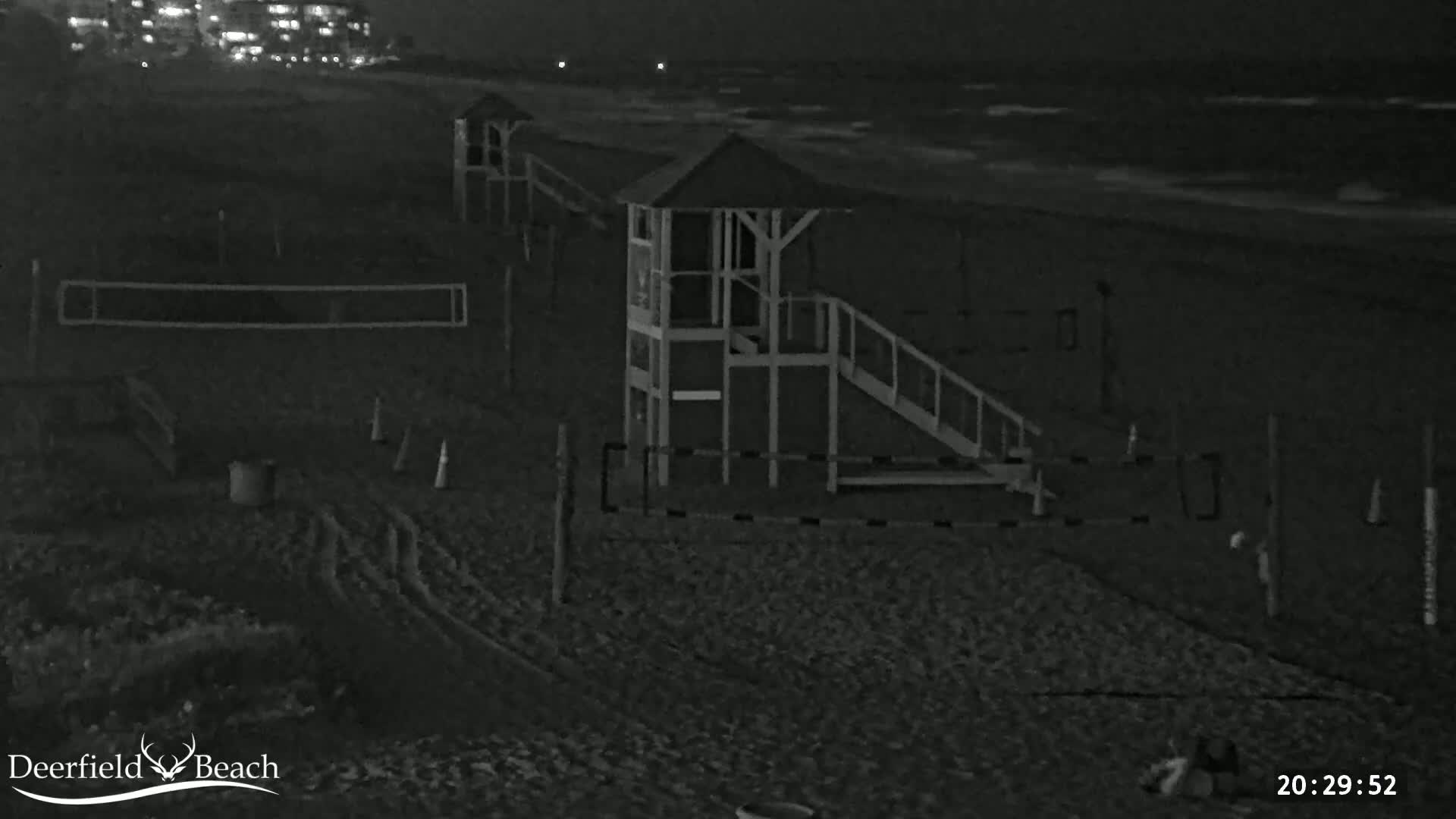 A nighttime view of a beach showing a lifeguard stand, volleyball net, and calm ocean waves.