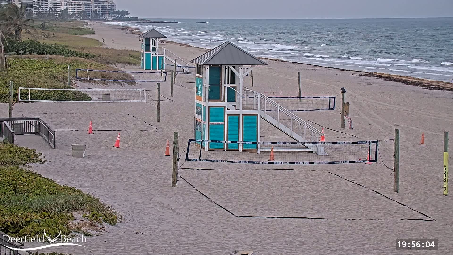Several volleyball courts are set up on a sandy beach near the ocean under an overcast sky.
