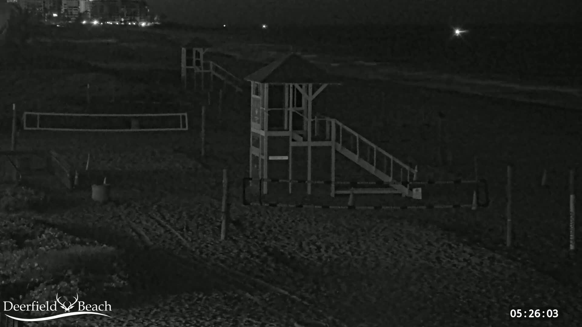A lifeguard stand with a slide and volleyball net sits on a dark beach at night.