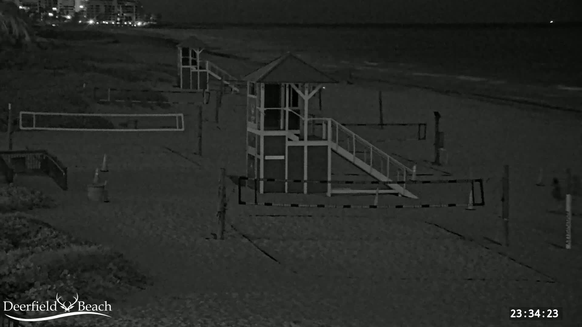 A nighttime view of a sandy beach shows a lifeguard stand and volleyball nets under dark, nighttime conditions.