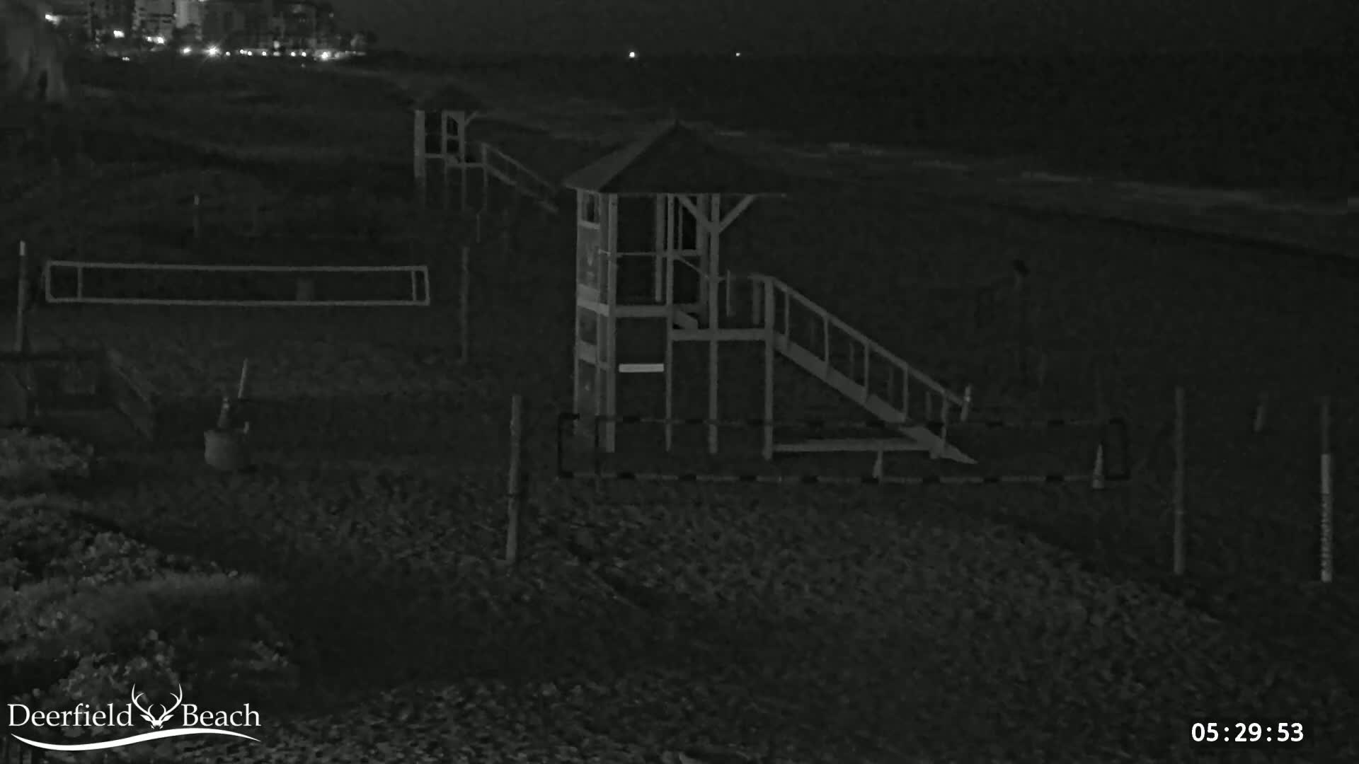 A dark, nighttime beach scene shows a lifeguard stand, a volleyball net, and a calm ocean under a clear sky.