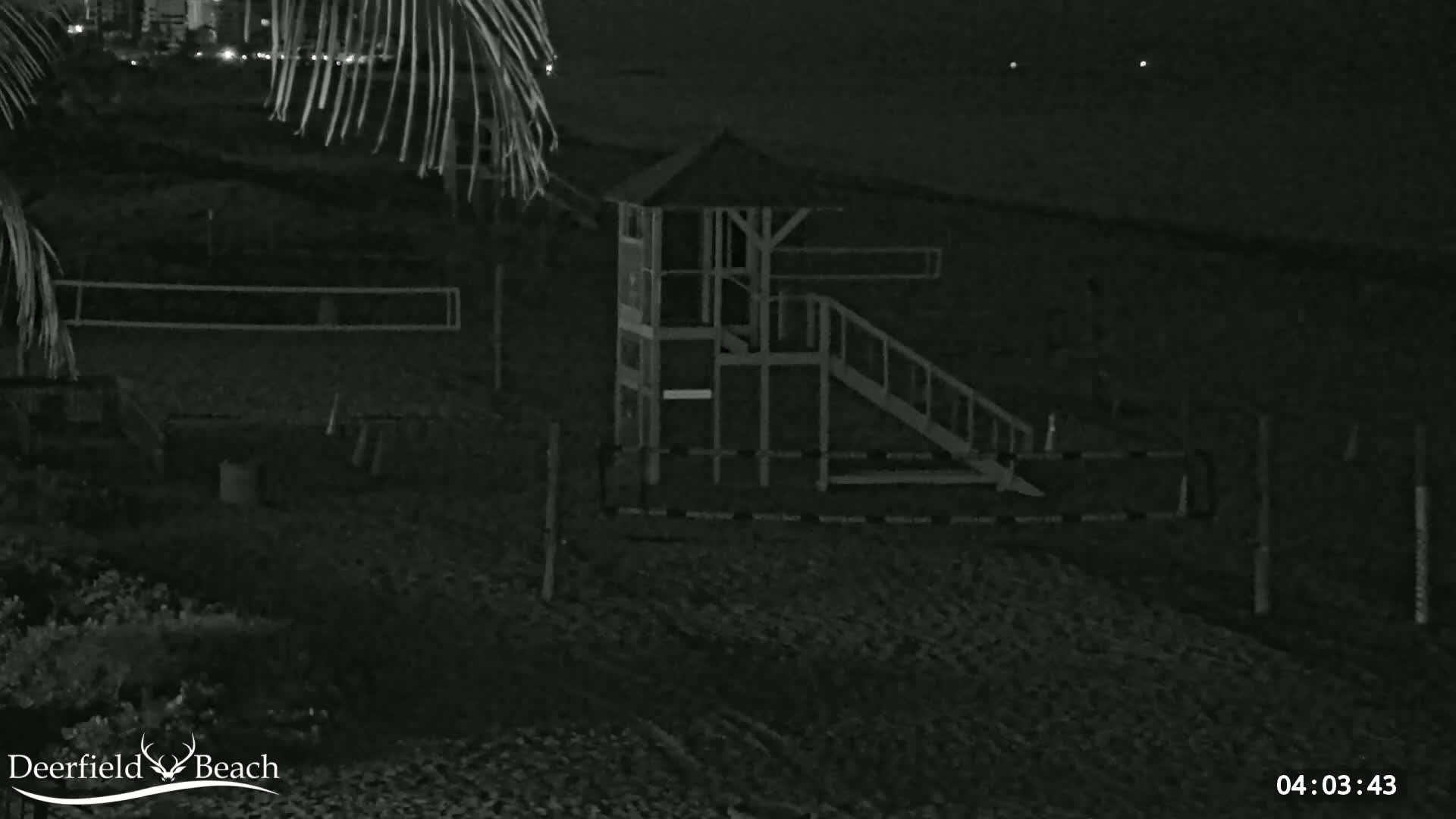 A nighttime, low-light image shows a lifeguard stand and volleyball net on a dark sandy beach.