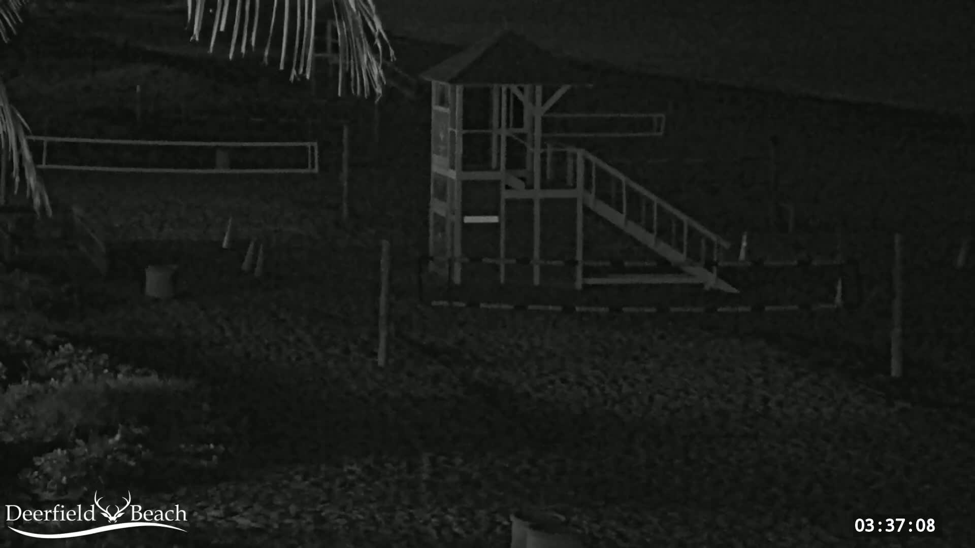 A nighttime, low-light image shows a playground structure with a slide and a small tower on a sandy beach.