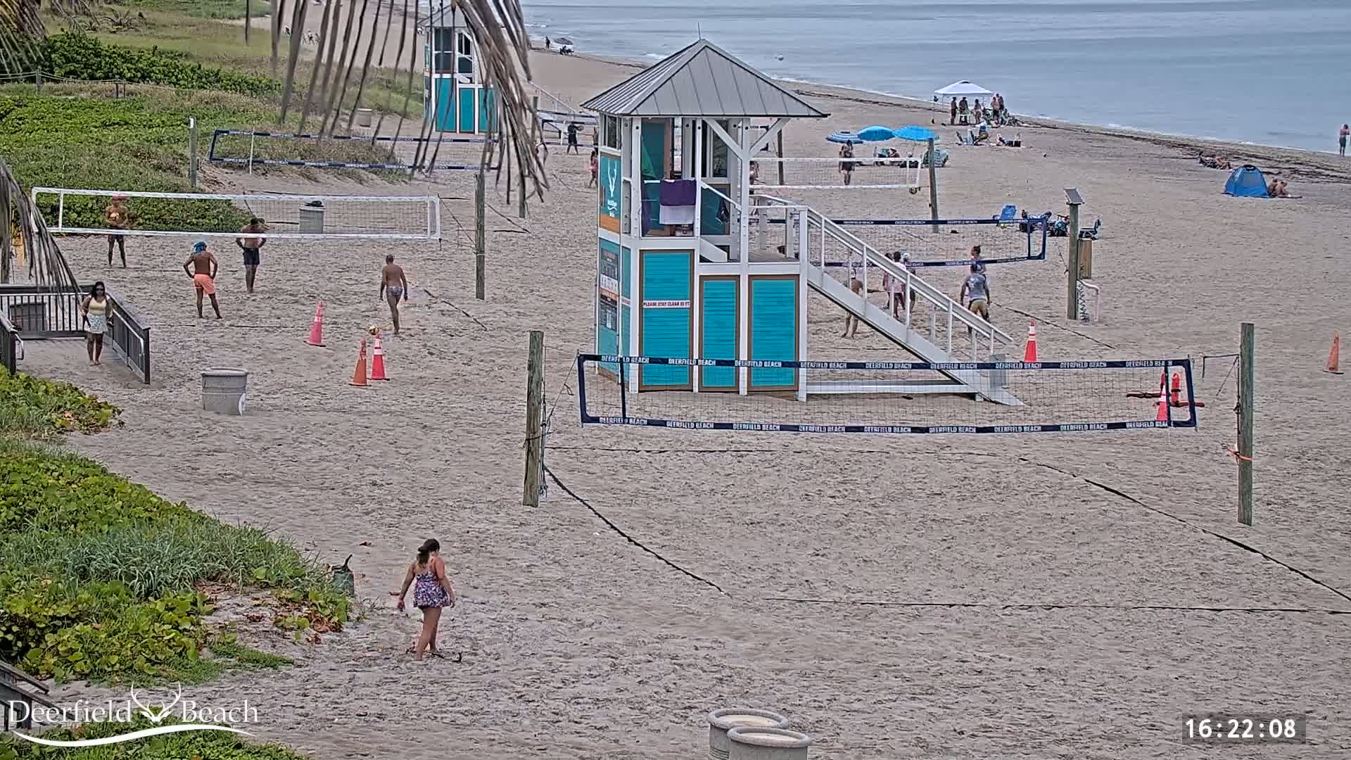 Several people are playing volleyball on a sandy beach near a lifeguard stand under an overcast sky.
