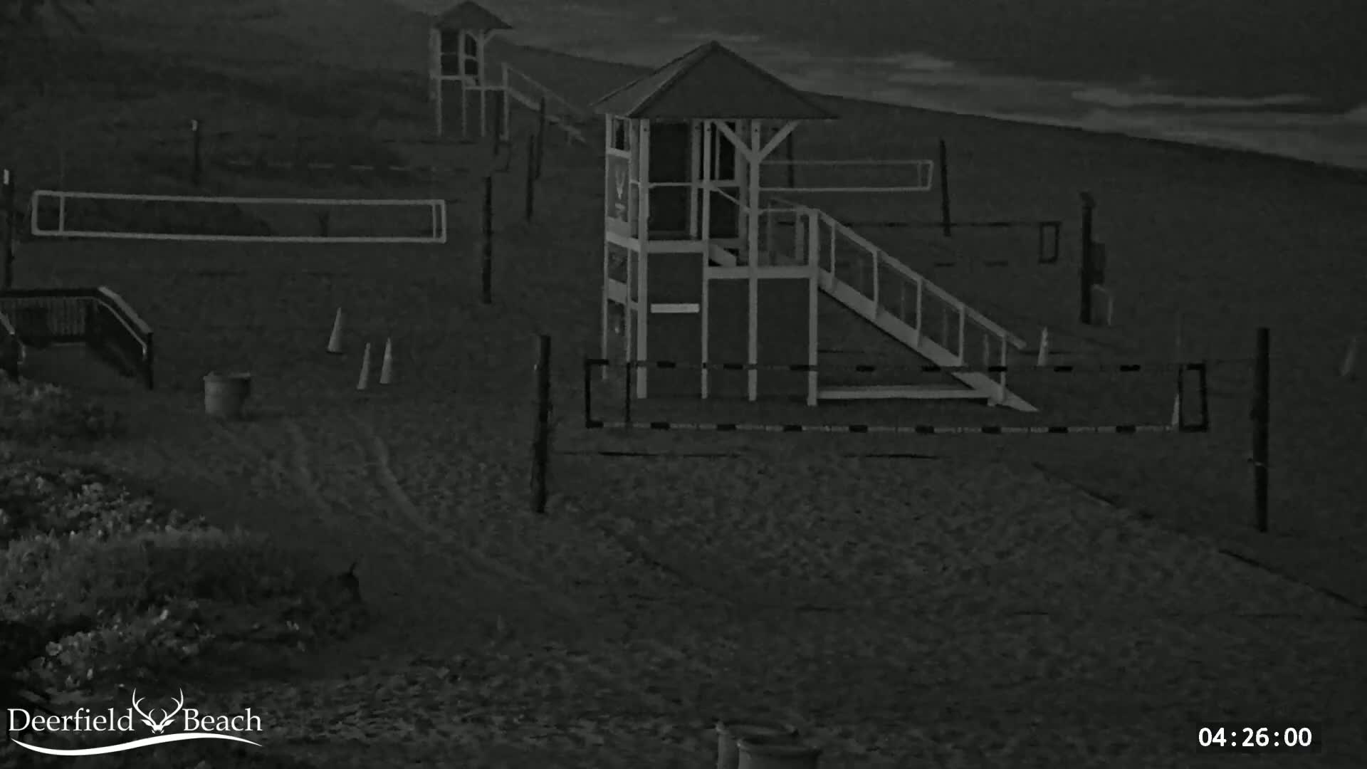 A nighttime, low-light view of a sandy beach showing volleyball nets, lifeguard stands, and other beach equipment.