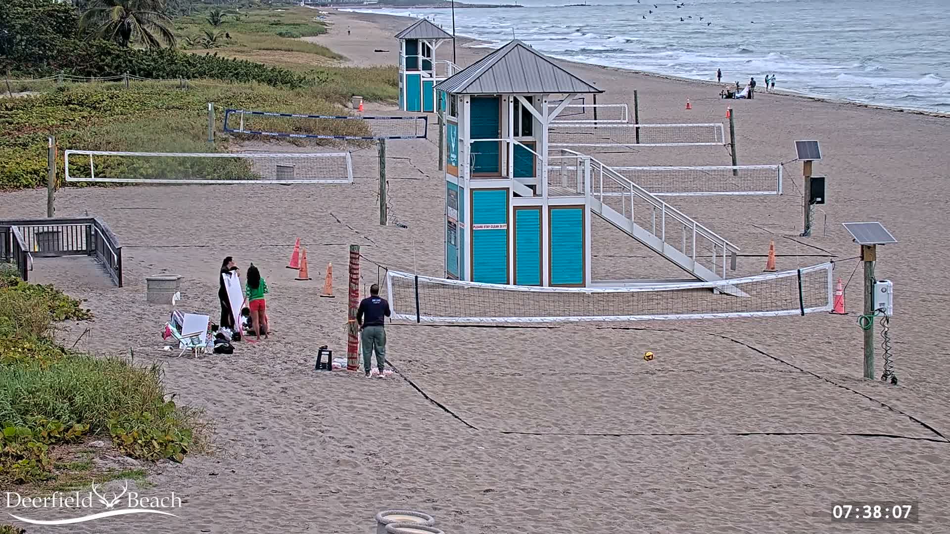 A dark, clear night reveals a sandy beach with two volleyball courts, two observation towers, and the ocean with visible waves along the right edge.