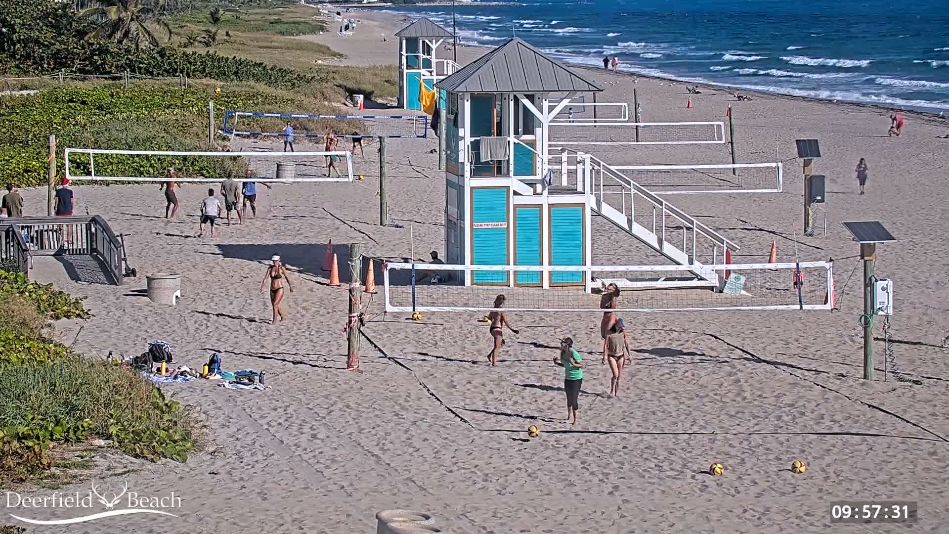 A dark, clear night reveals a sandy beach with two volleyball courts, two observation towers, and the ocean with visible waves along the right edge.