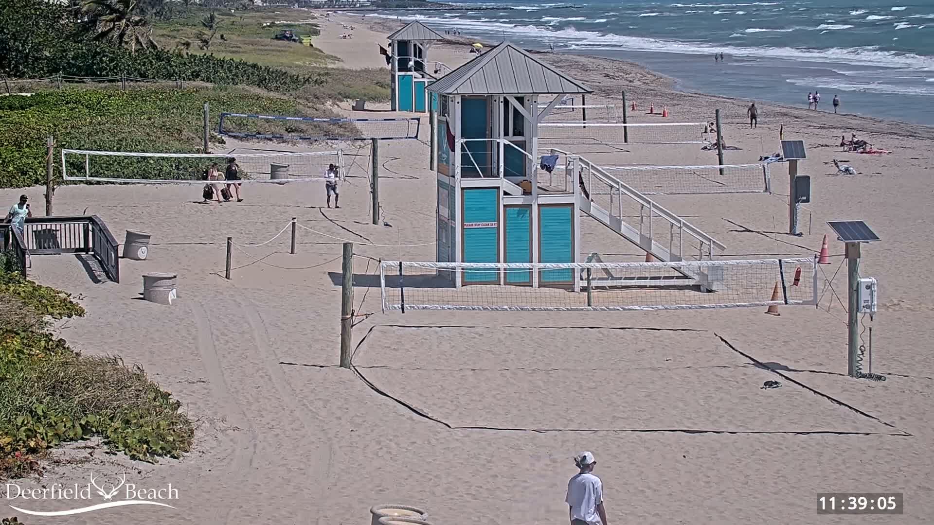 A dark, clear night reveals a sandy beach with two volleyball courts, two observation towers, and the ocean with visible waves along the right edge.