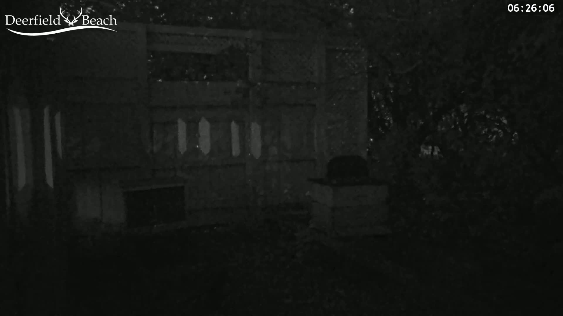 A low-light nighttime image shows a dark structure with several windows, a fireplace, and what appears to be a grill or outdoor cooking area.