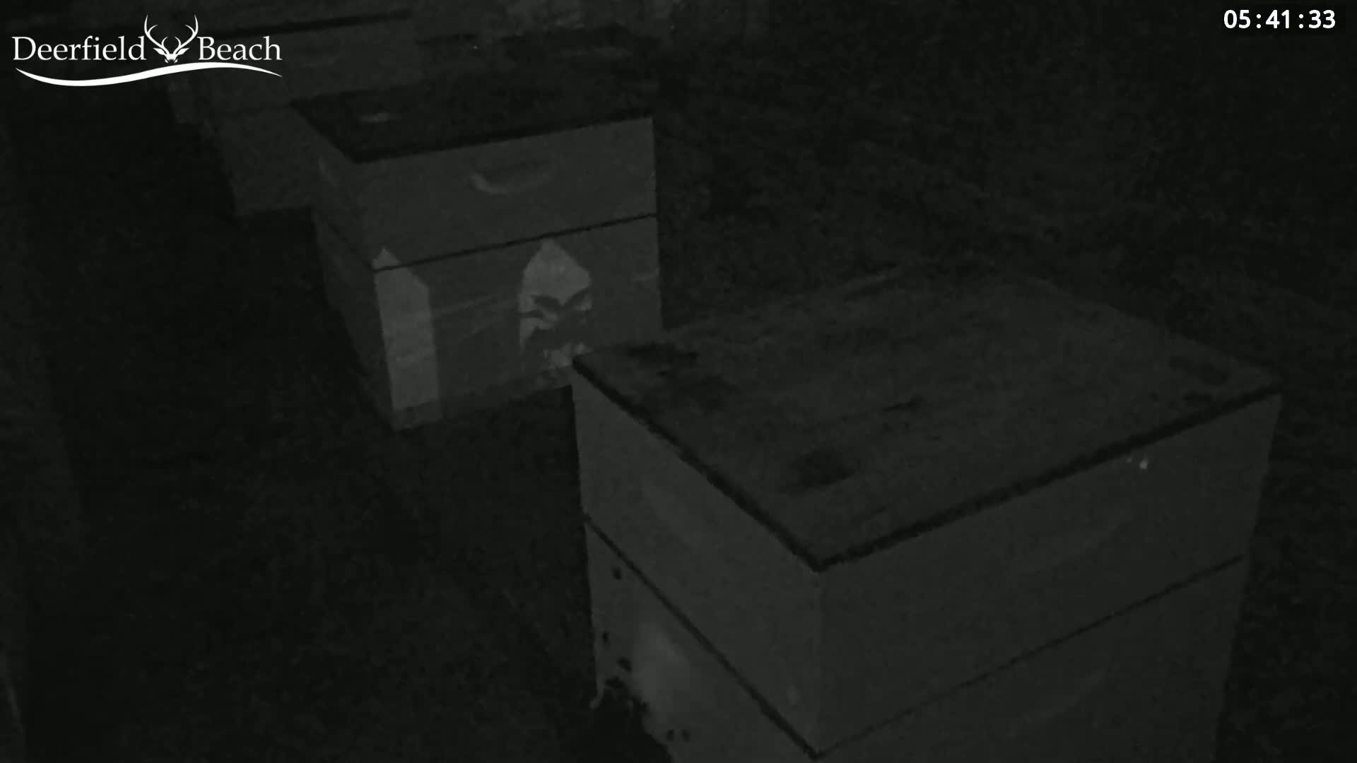 A nighttime, low-light image shows two dark rectangular objects, possibly boxes, stacked near each other.