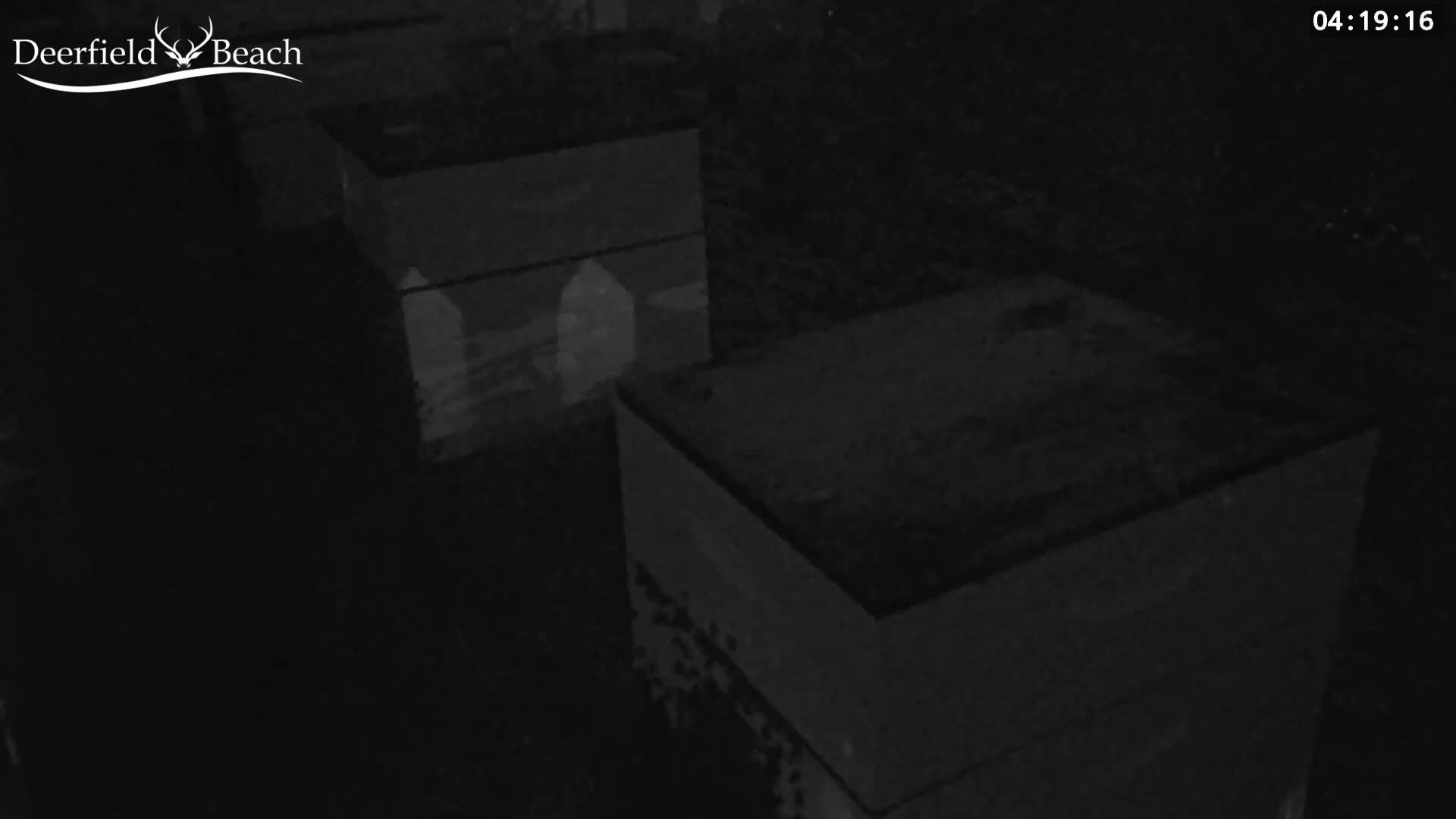 Two dark, rectangular objects, possibly boxes or containers, are visible in a low-light, nighttime setting.
