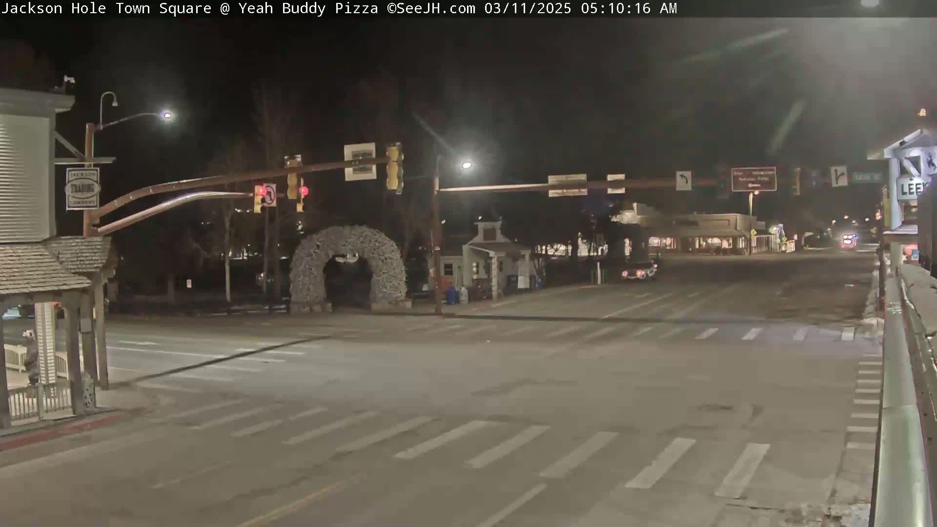 A nighttime view of a town square intersection with a few cars, streetlights, and a decorative archway.
