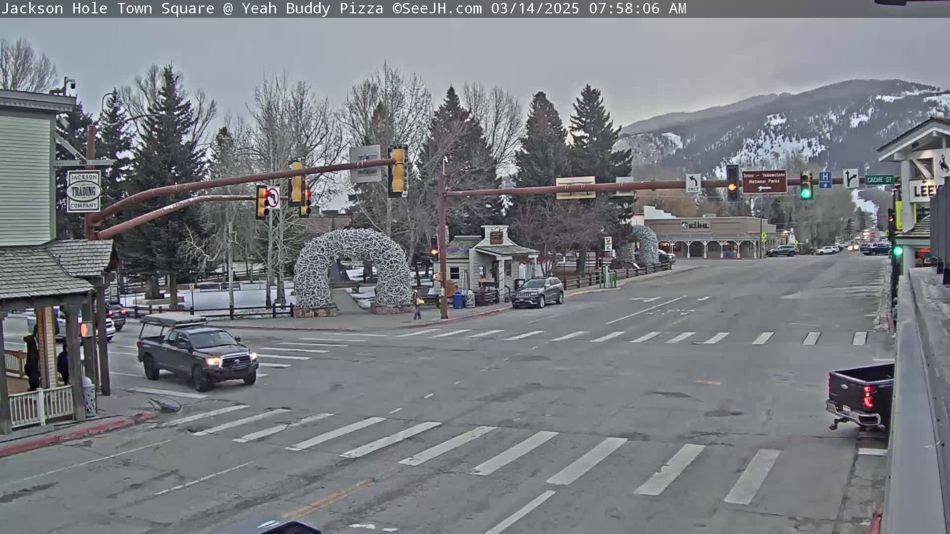 A town square intersection with sparse traffic under an overcast sky, featuring a large antler arch and several buildings.