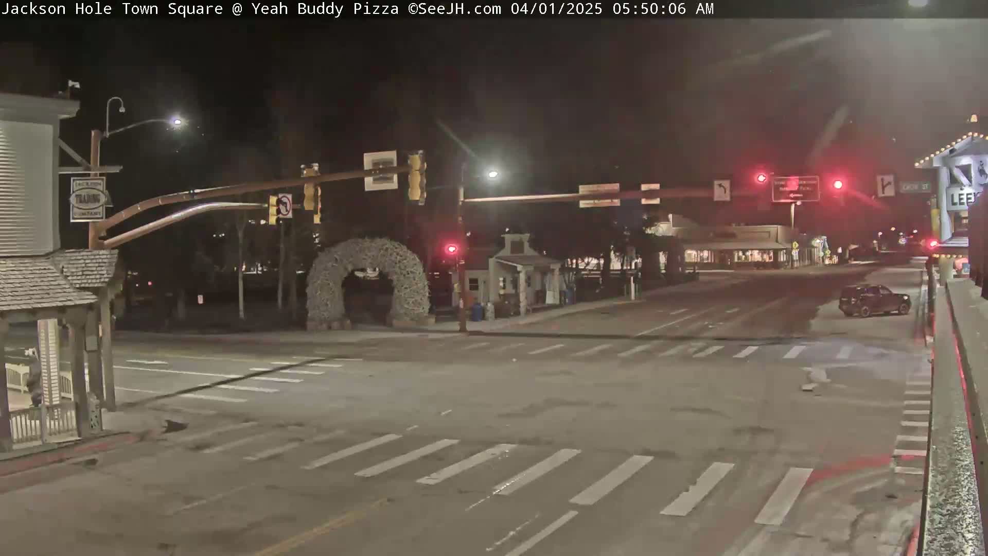 A nighttime view of a mostly empty town square intersection with a single vehicle parked at the side of the road.